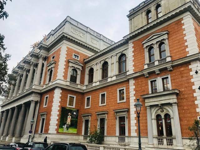 Prachtvolles historisches Gebäude mit orangeroter Fassade, klassischen Säulen und vielen Fenstern an einer Stadtstraße.
