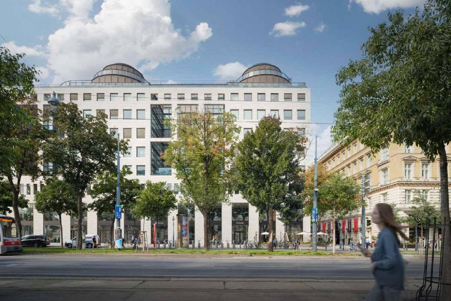 Moderne Gebäudefassade mit vielen Fenstern und Bäumen entlang einer belebten Straße in einer städtischen Umgebung am Tag.
