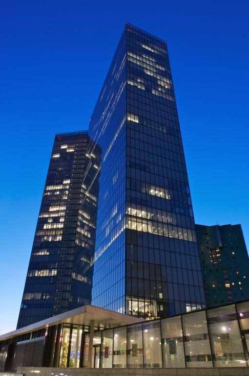 Moderne Hochhäuser mit Glasfassaden bei Dämmerung, beleuchtet und imposant in der Stadtlandschaft.