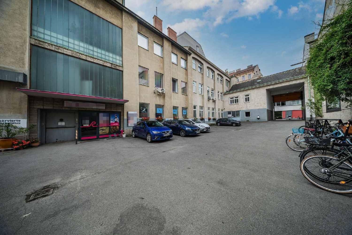 Außenansicht eines Gewerbegebäudes mit Parkplätzen und Fahrrädern im Vordergrund, zeigt den Eingangsbereich.