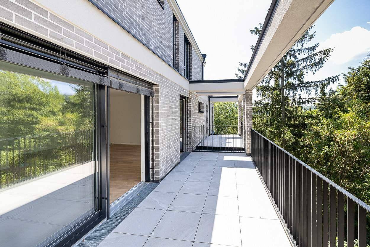 Lange, moderne Terrasse mit grauen Fliesen und Blick auf die umliegende grüne Landschaft.