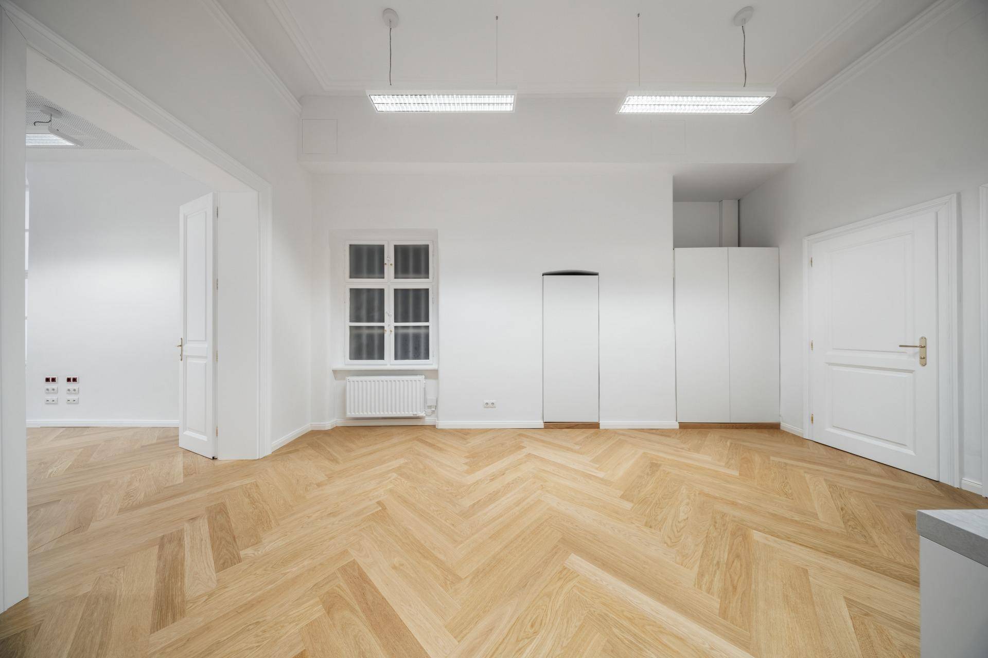 Heller, leerer Raum mit Fischgrätparkett, Fenster und integrierten weißen Schränken.