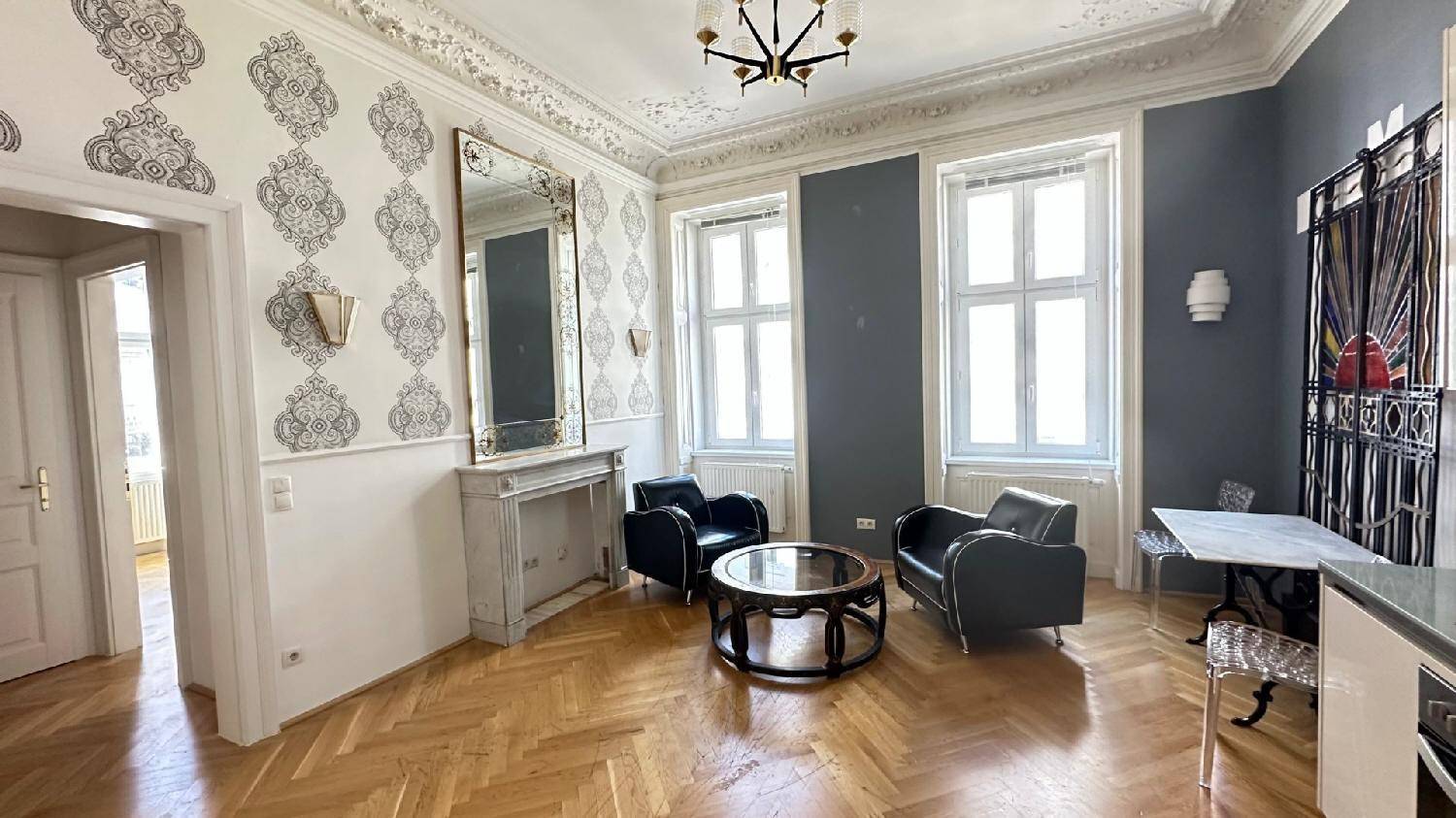 Elegantes Wohnzimmer mit Fischgrätparkett, Stuckdecke und großem Spiegel über dem Kaminsims.
