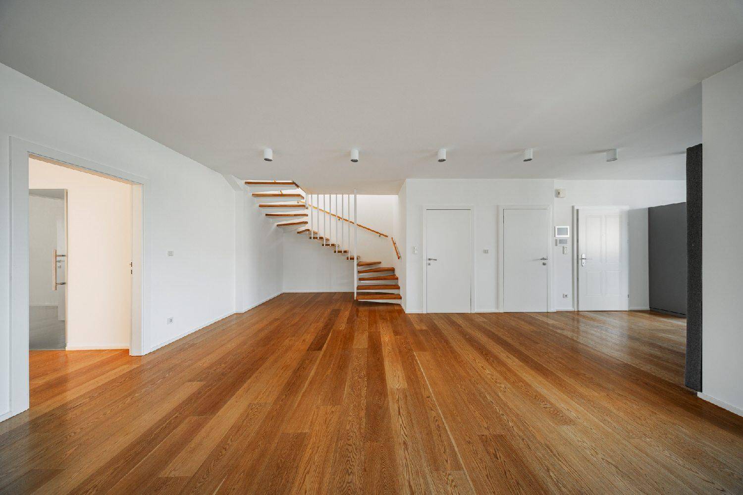 Geräumiger Wohnbereich mit Holzboden und eleganter Holztreppe, die die Ebenen verbindet.