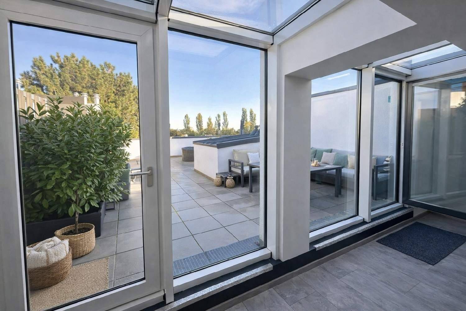 Heller Wintergarten mit großen Glasfronten und direktem Zugang zur sonnigen Dachterrasse.