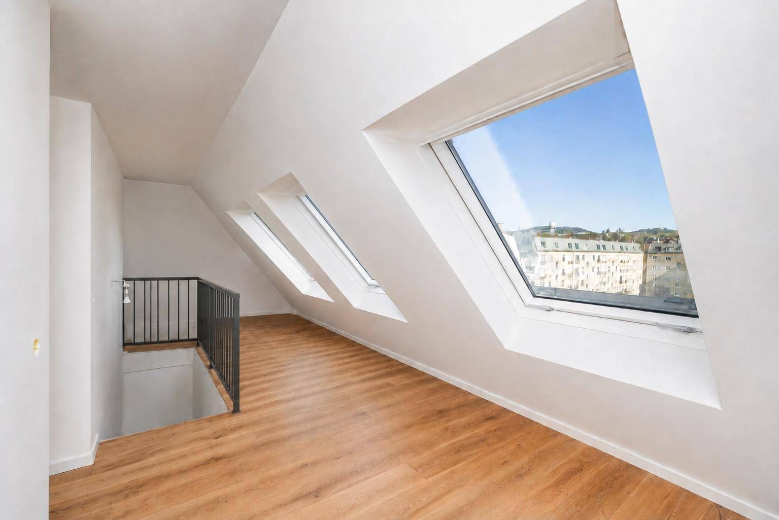 Heller Dachbodenraum mit schrägen Wänden, Laminatboden und Blick über die Stadt.
