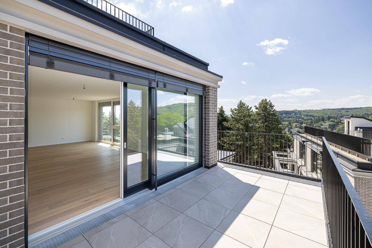 Sonniger Balkon mit Fliesenboden, Blick auf die grüne Landschaft und Zugang zum Innenbereich.