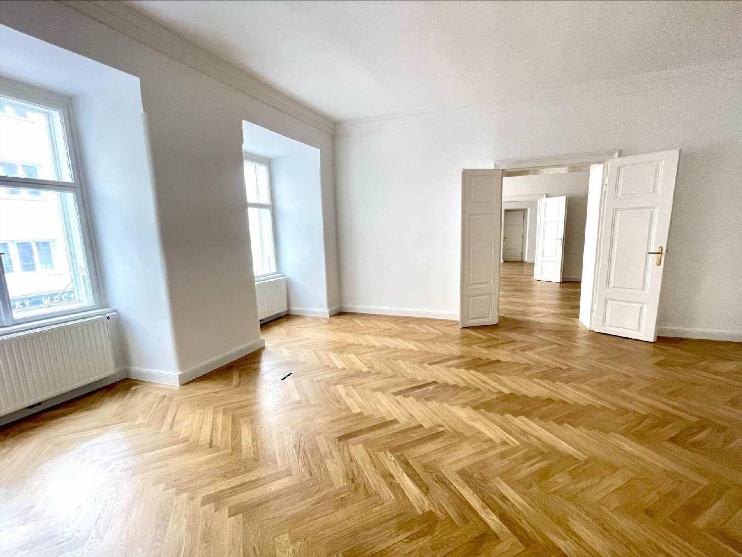 Geräumiges Wohnzimmer mit Fischgrätparkett, hohen Decken und großen Fenstern, die viel Tageslicht hereinlassen.