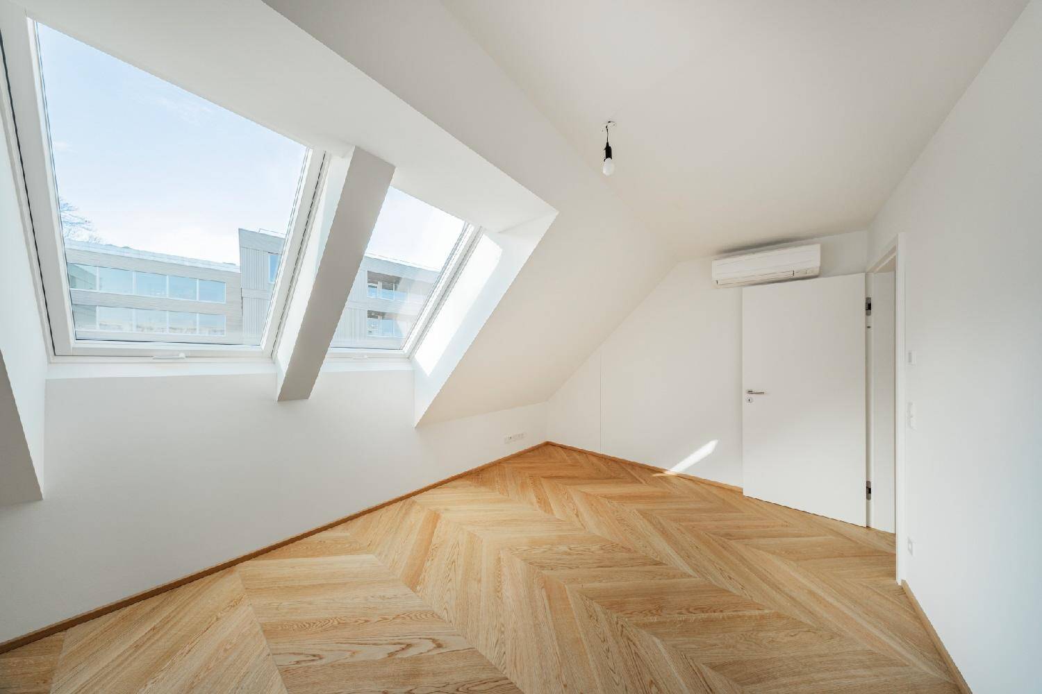 Helles Dachgeschosszimmer mit schrägen Wänden, zwei großen Dachfenstern und Holzparkettboden.