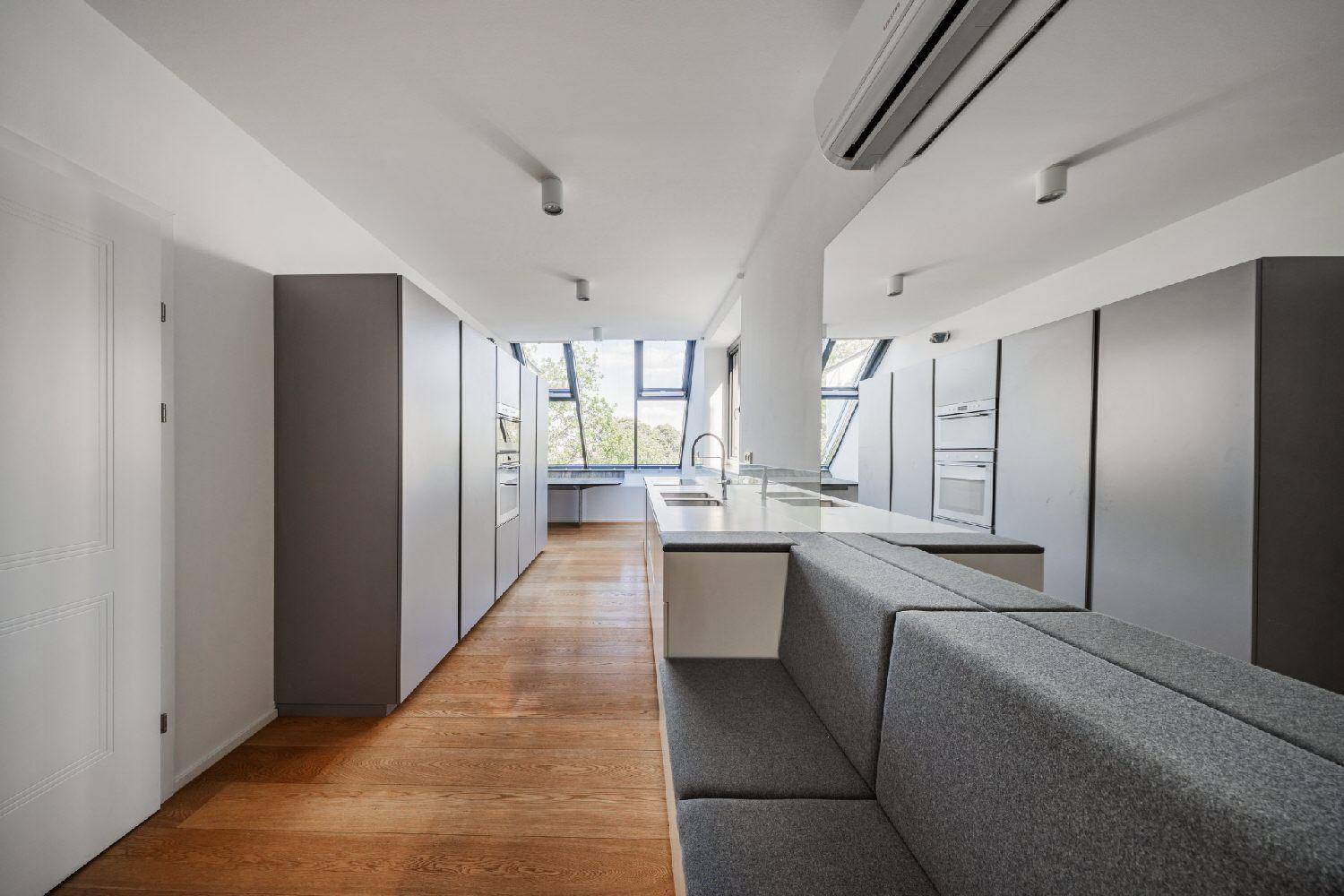 Offene Küche mit grauen Schränken, integrierter Sitzgelegenheit und Holzboden in einem modernen Ambiente.