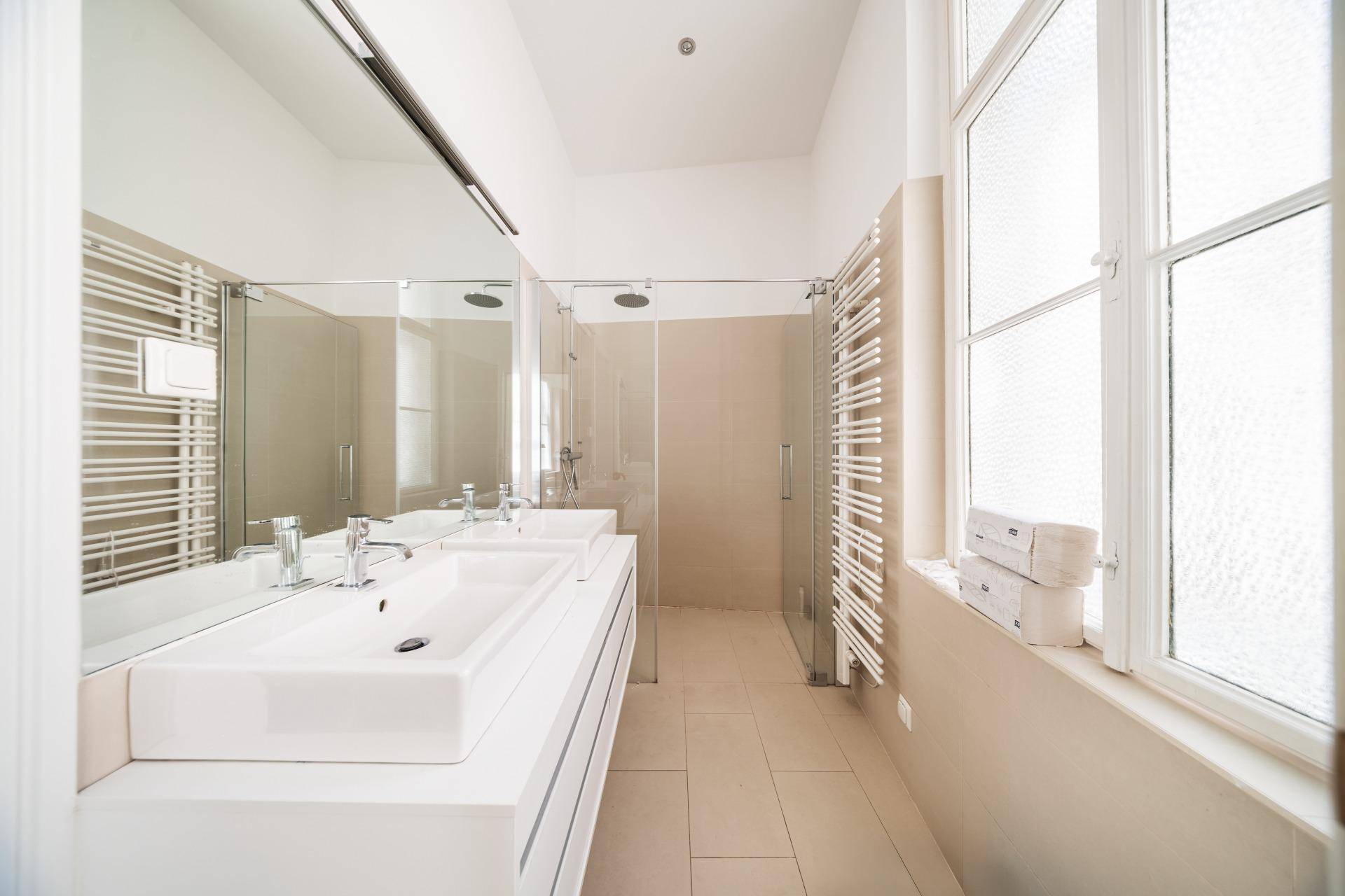 Modernes Badezimmer mit Doppelwaschbecken, großer Dusche und Fenster für Tageslicht.