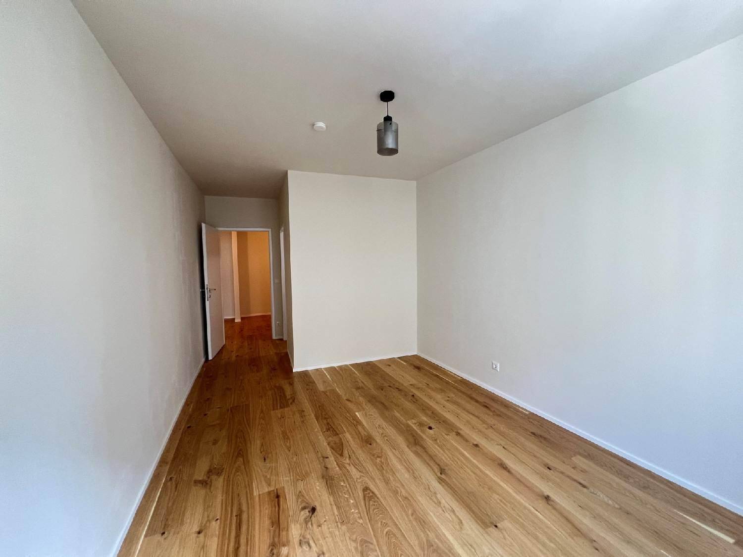 Helles Zimmer mit Holzparkettboden und Zugang zu einem angrenzenden Flur.