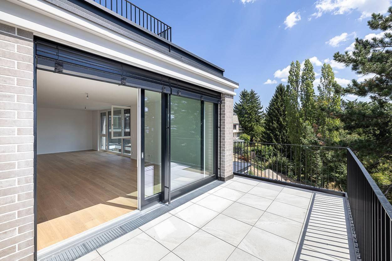 Heller Balkon mit Fliesenboden und Blick auf die grüne Umgebung sowie den Innenraum.