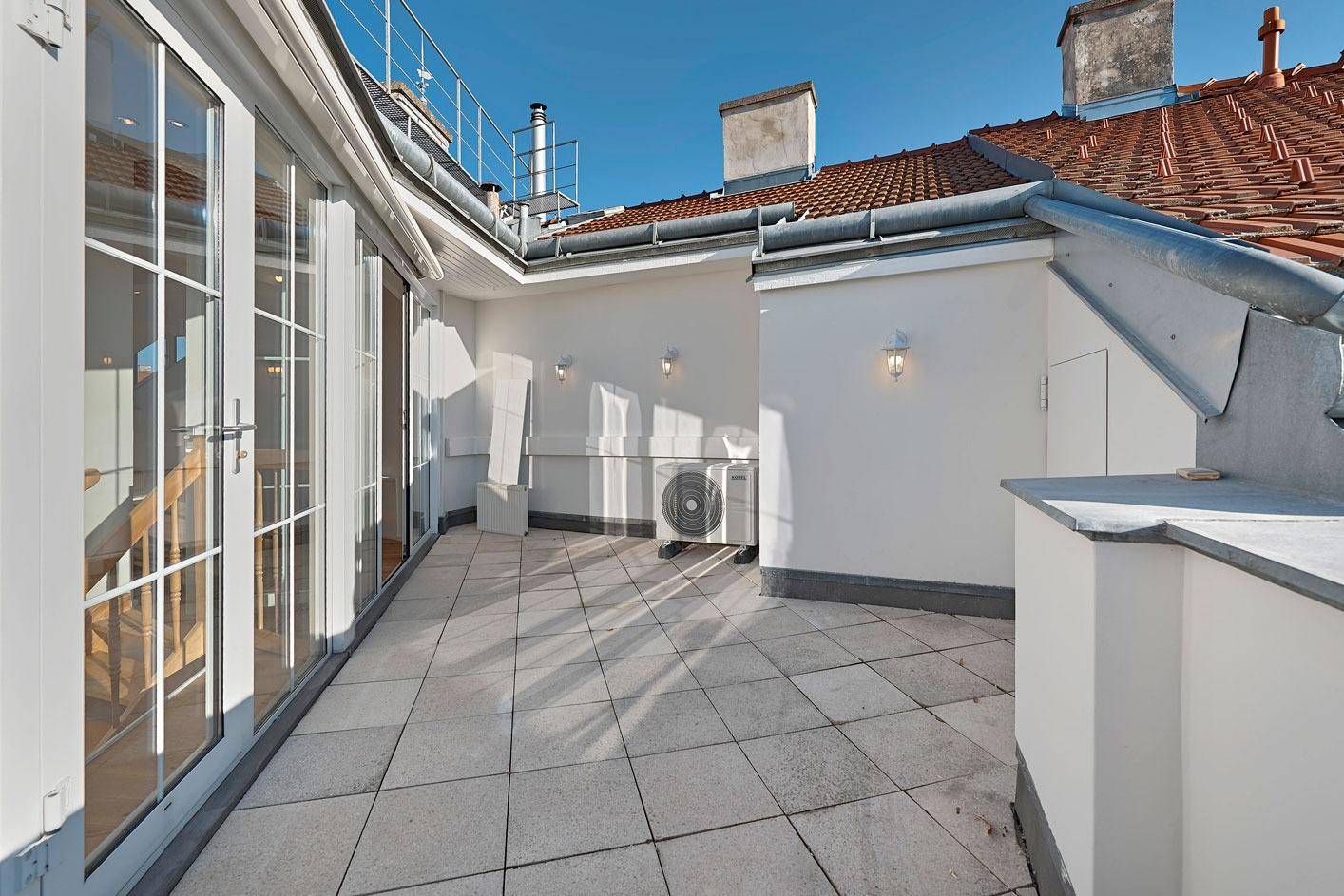 Geräumige Dachterrasse mit Fliesenboden und Blick über die Dächer der Stadt.