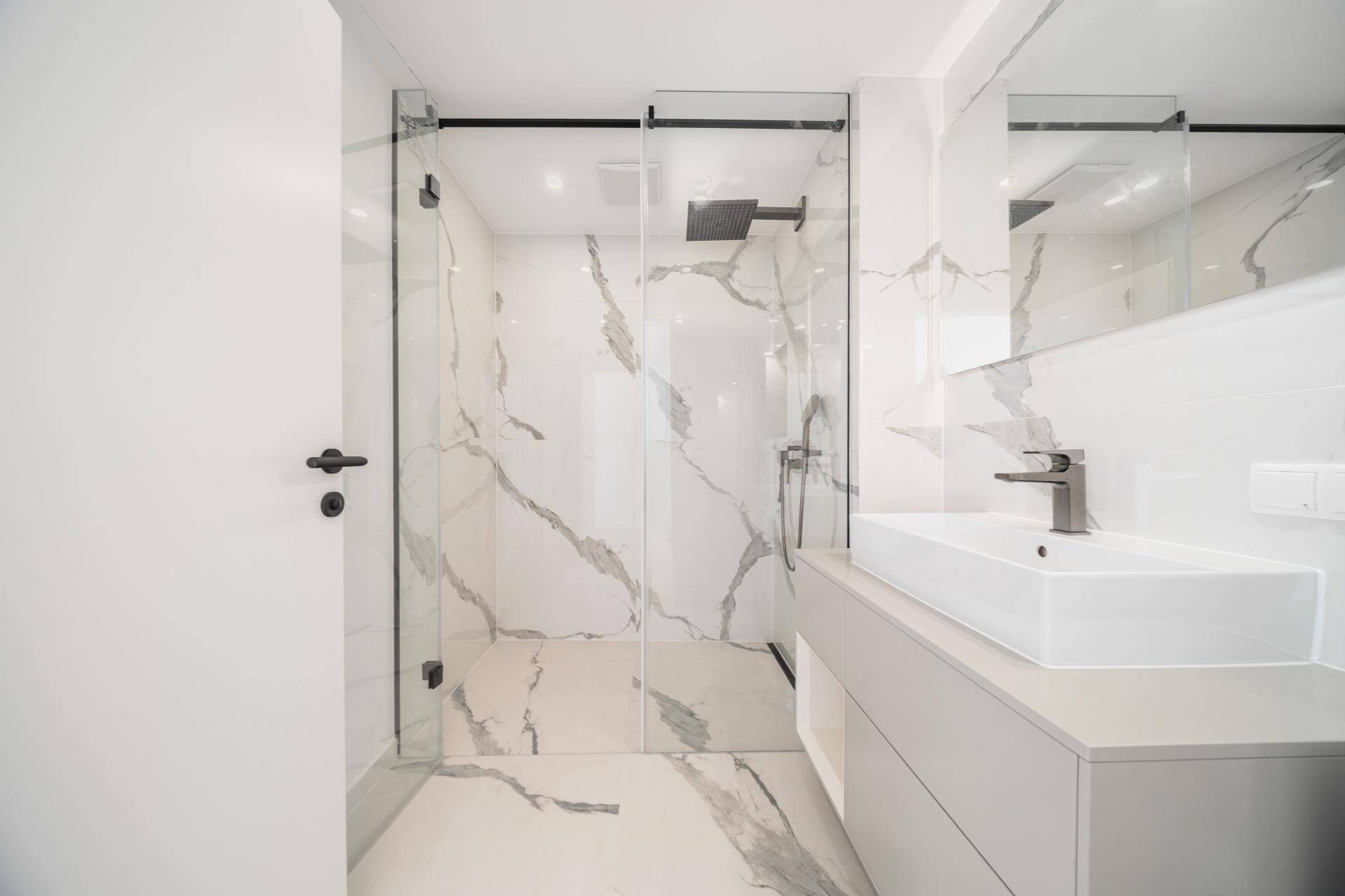 Elegantes Badezimmer mit großformatigen Marmorfliesen, modernem Waschbecken und geräumiger begehbarer Dusche.