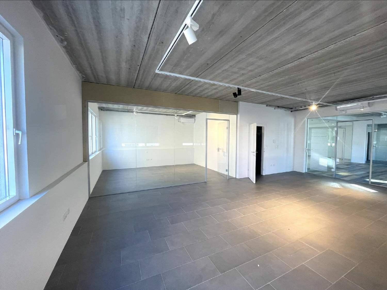 Leeres Büro mit dunklem Fliesenboden, Sichtbetondecke, großen Fenstern und Glaswänden.