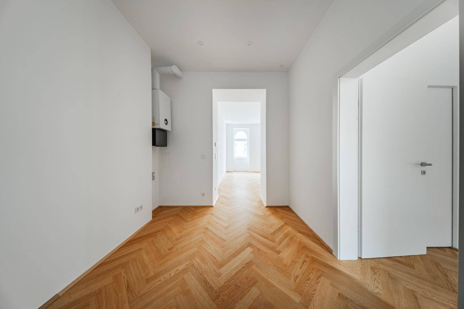 Heller Flur mit Fischgrätparkett und einem Heizkessel an der Wand.
