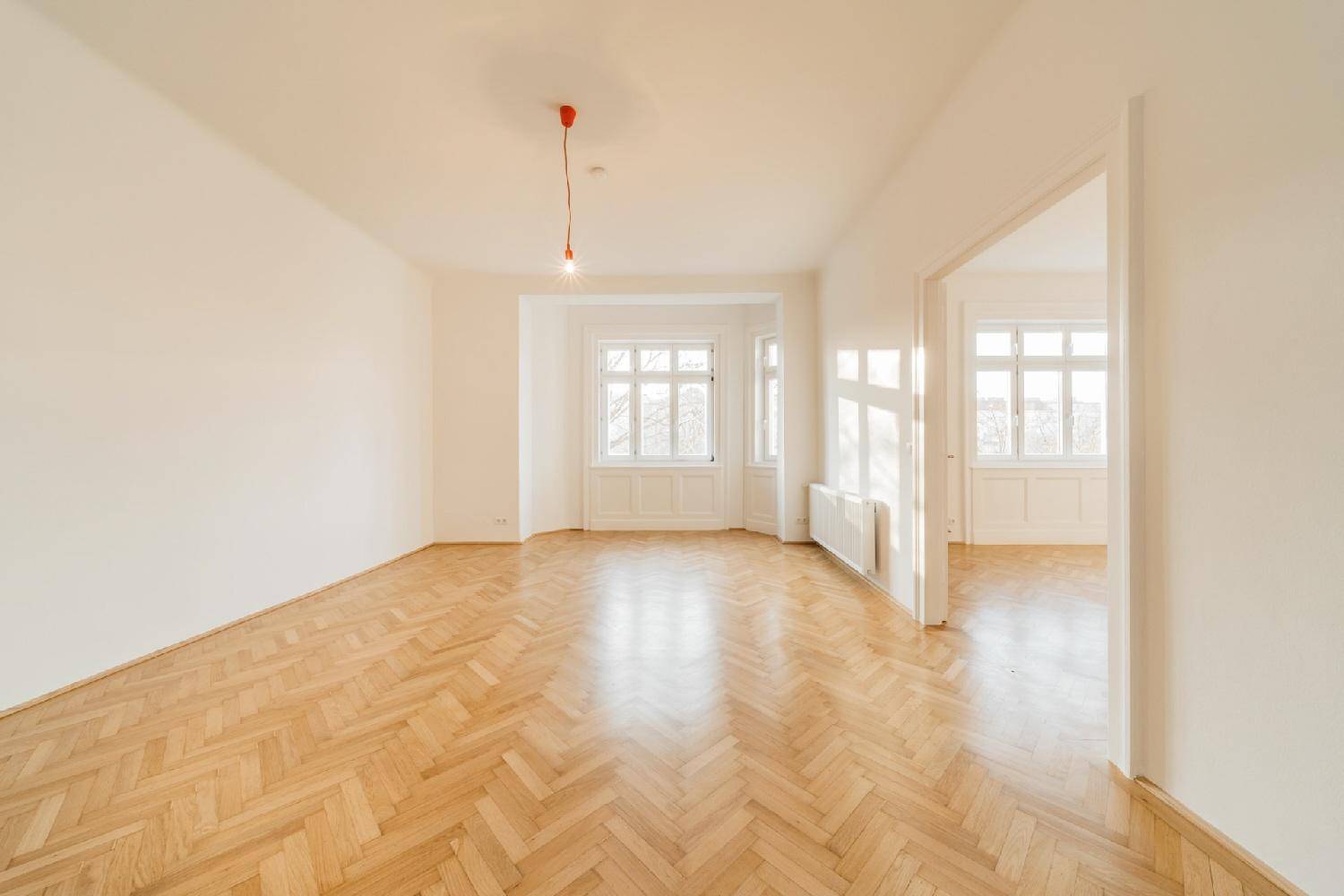 Lichtdurchfluteter Wohnbereich mit elegantem Fischgrätparkett und hohen Decken, bereit zur individuellen Gestaltung.