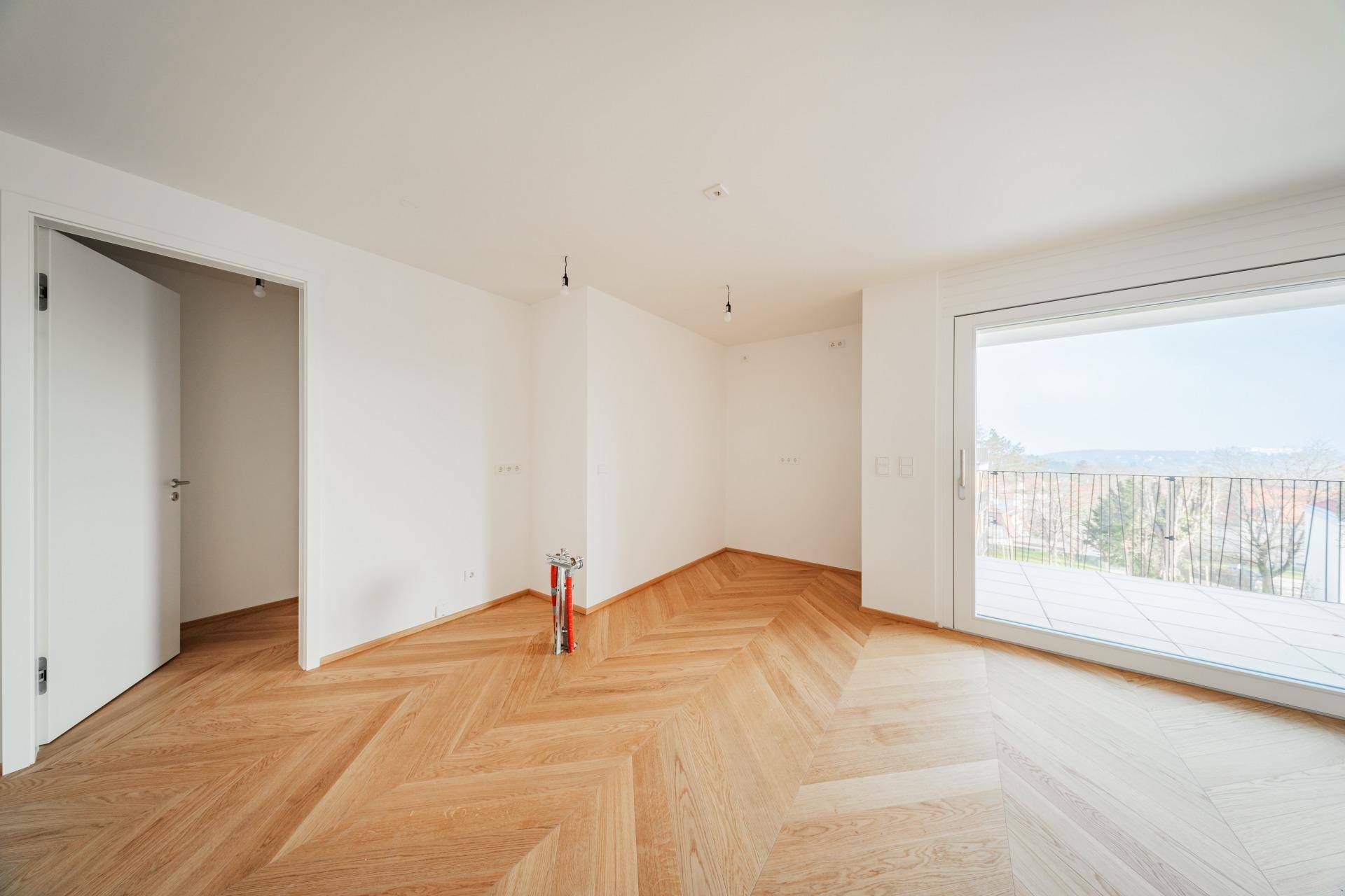 Heller Wohnraum mit Fischgrät-Parkettboden und großzügigem Zugang zu einer Außenterrasse oder Balkon.