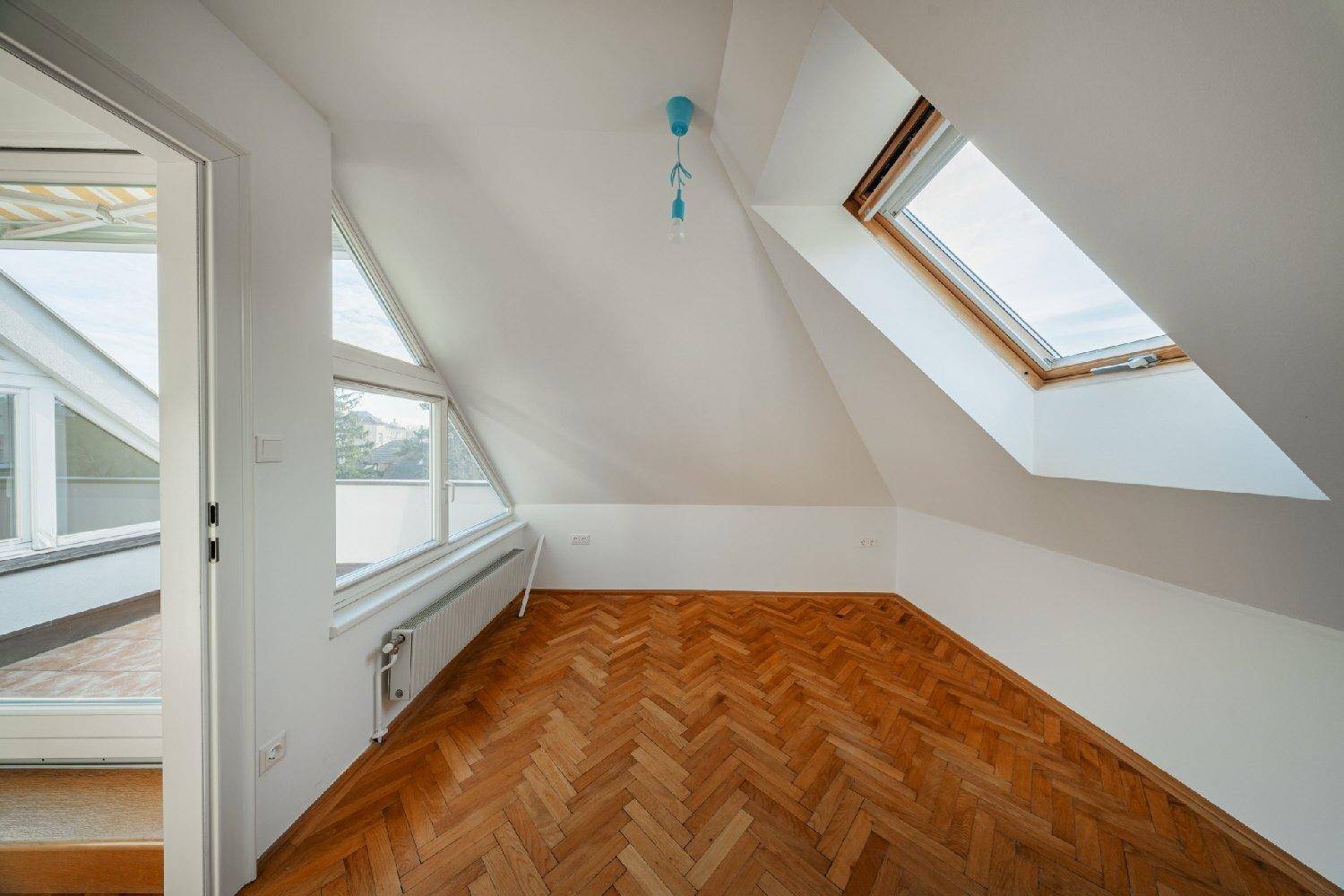 Helles Dachzimmer mit schrägen Wänden, Dachfenster und einem weiteren Fenster für viel Licht.