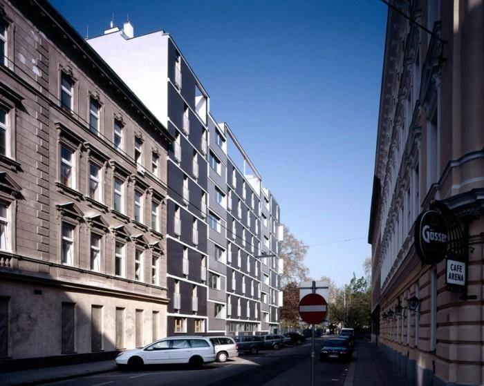 Lange Fassade eines modernen Wohnhauses in einer städtischen Umgebung unter klarem blauem Himmel.