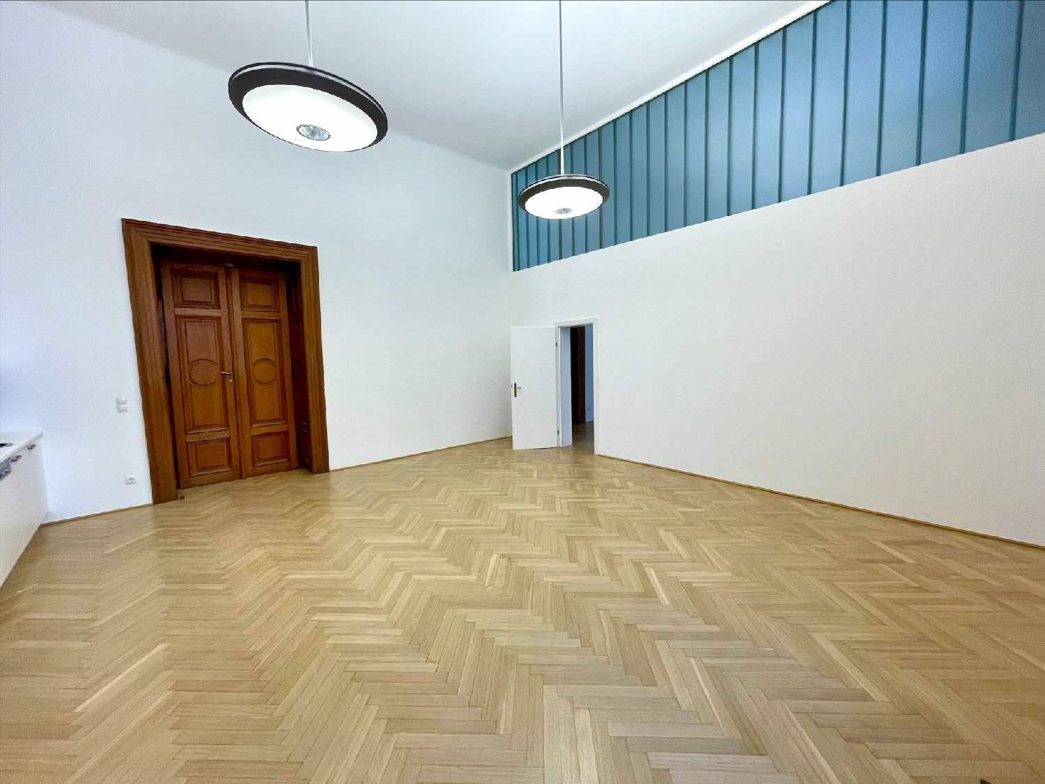 Geräumiger Büroraum mit Fischgrätparkett, hohen Decken und einer blauen Glaswand im oberen Bereich.