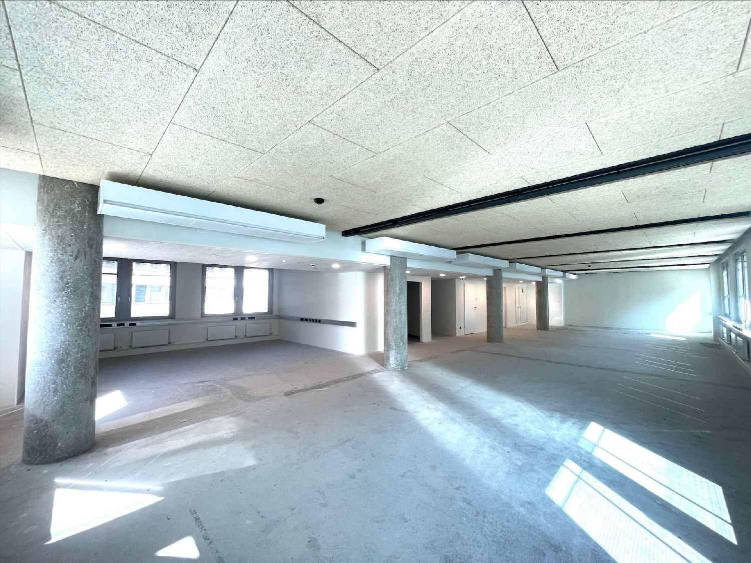 Weitläufiger, unmöblierter Büroraum mit mehreren Säulen, Betonboden und Akustikdeckenplatten, bereit zur individuellen Nutzung.