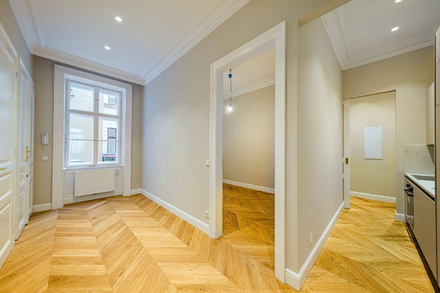 Flur mit Fischgrätparkett, der zu einem hellen Zimmer mit Fenster und einer modernen Küche führt.