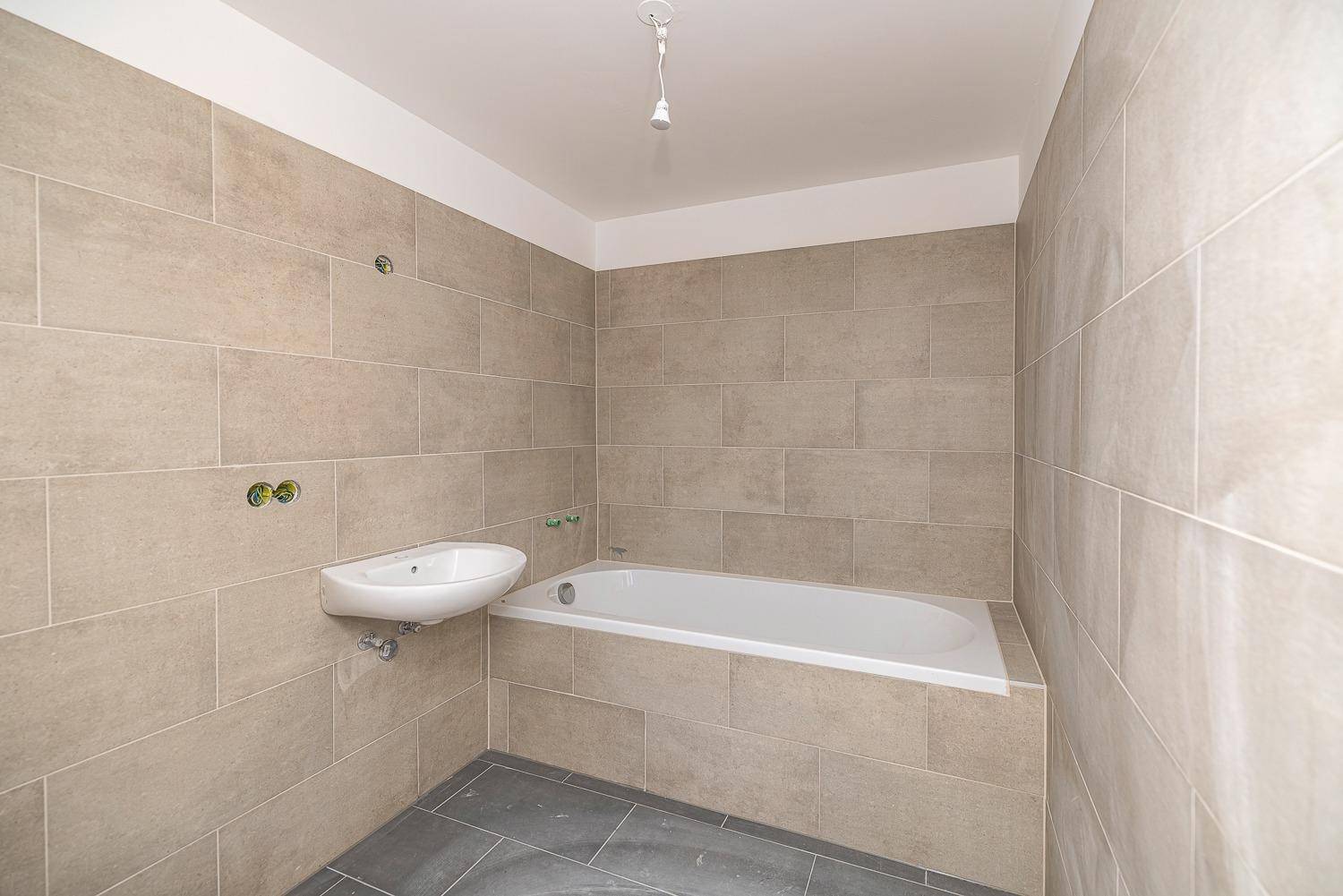 Modernes Badezimmer im Rohbau mit Badewanne und beigefarbenen Wandfliesen.