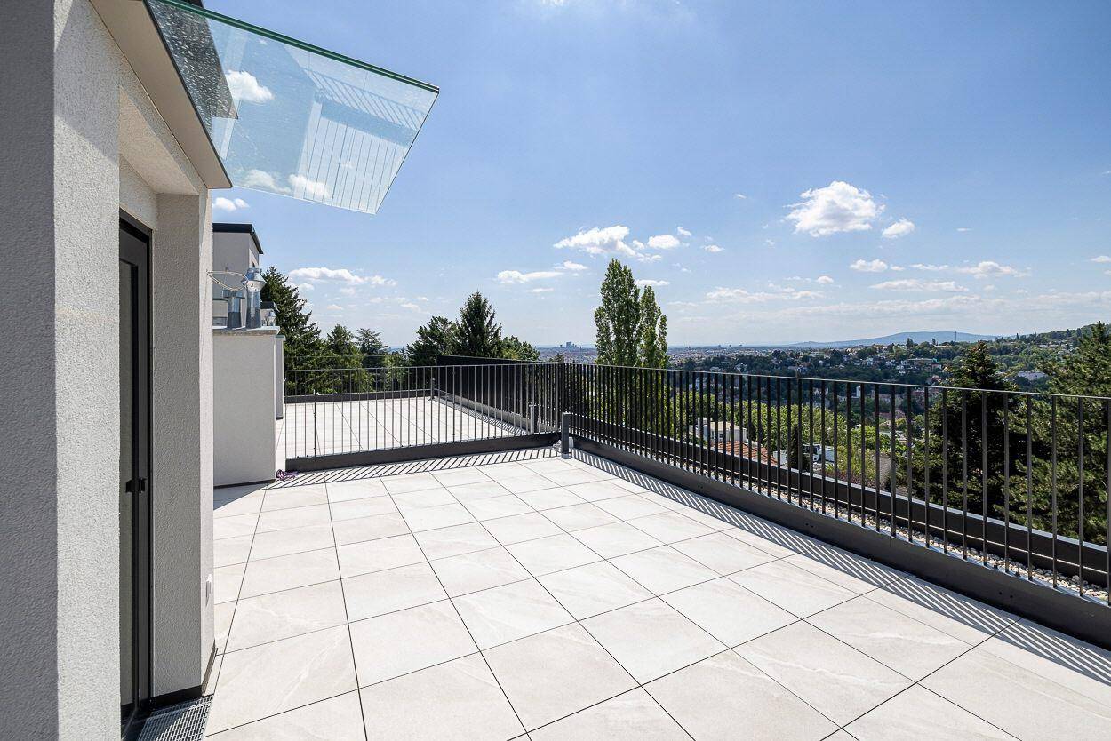 Große, sonnige Dachterrasse mit Fliesenboden, Metallgeländer und weitem Blick über die Landschaft.