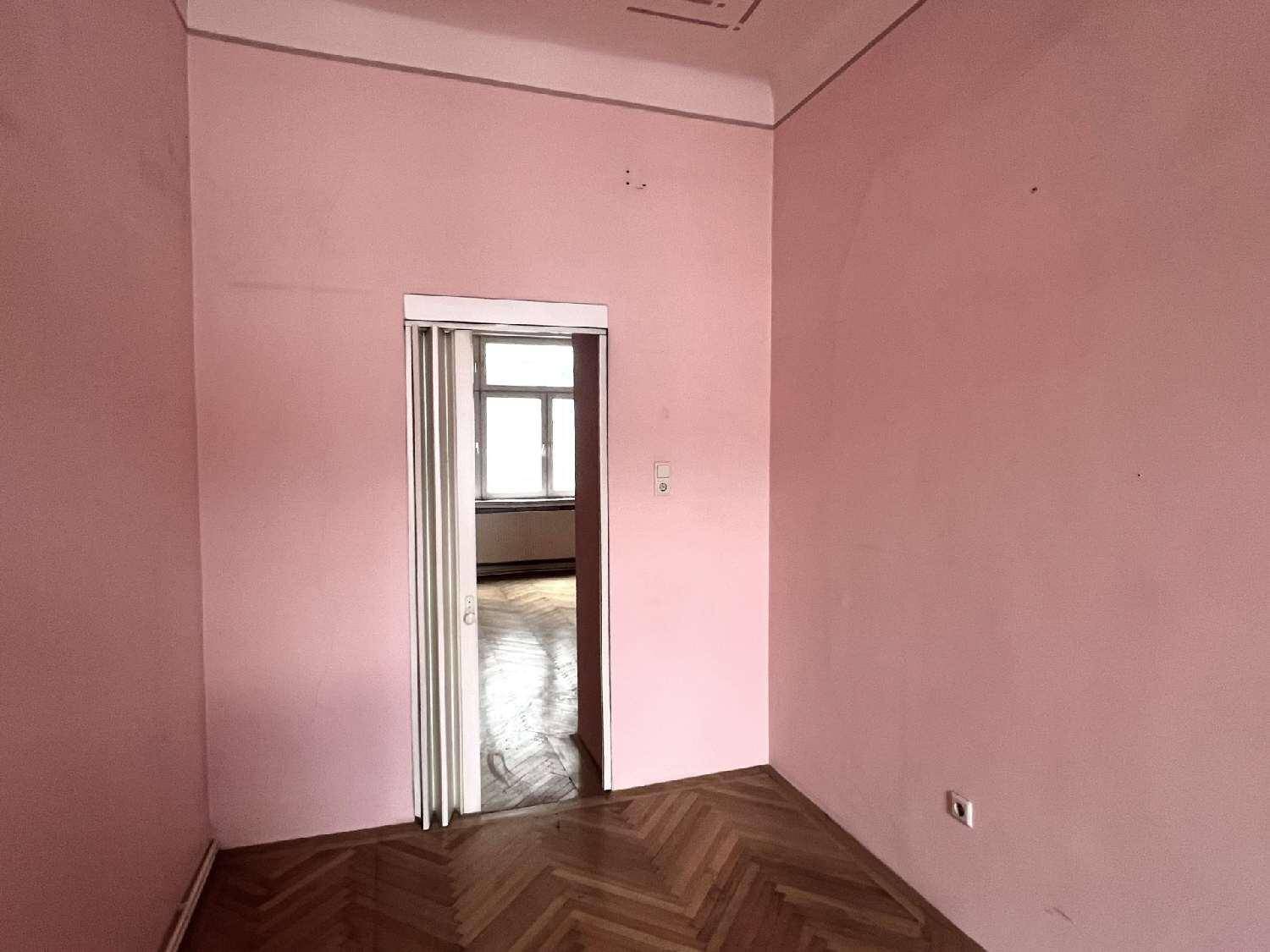 Leeres Zimmer mit Fischgrätparkett und rosa Wänden, mit Falttür zu einem Nebenraum.