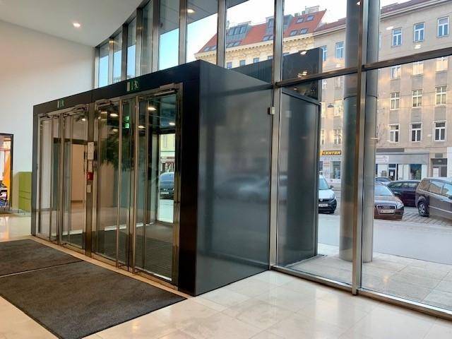 Heller Eingangsbereich mit großen Glasfenstern, die den Blick nach draußen freigeben, und Aufzügen.