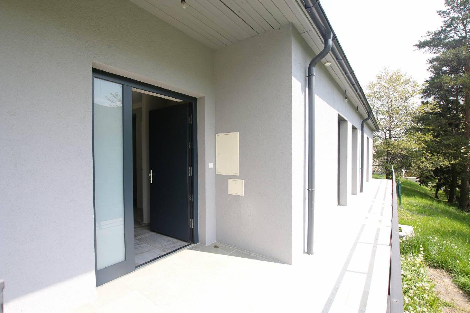 Moderner Eingangsbereich des Hauses mit großen Glastüren und schlichter Fassade.