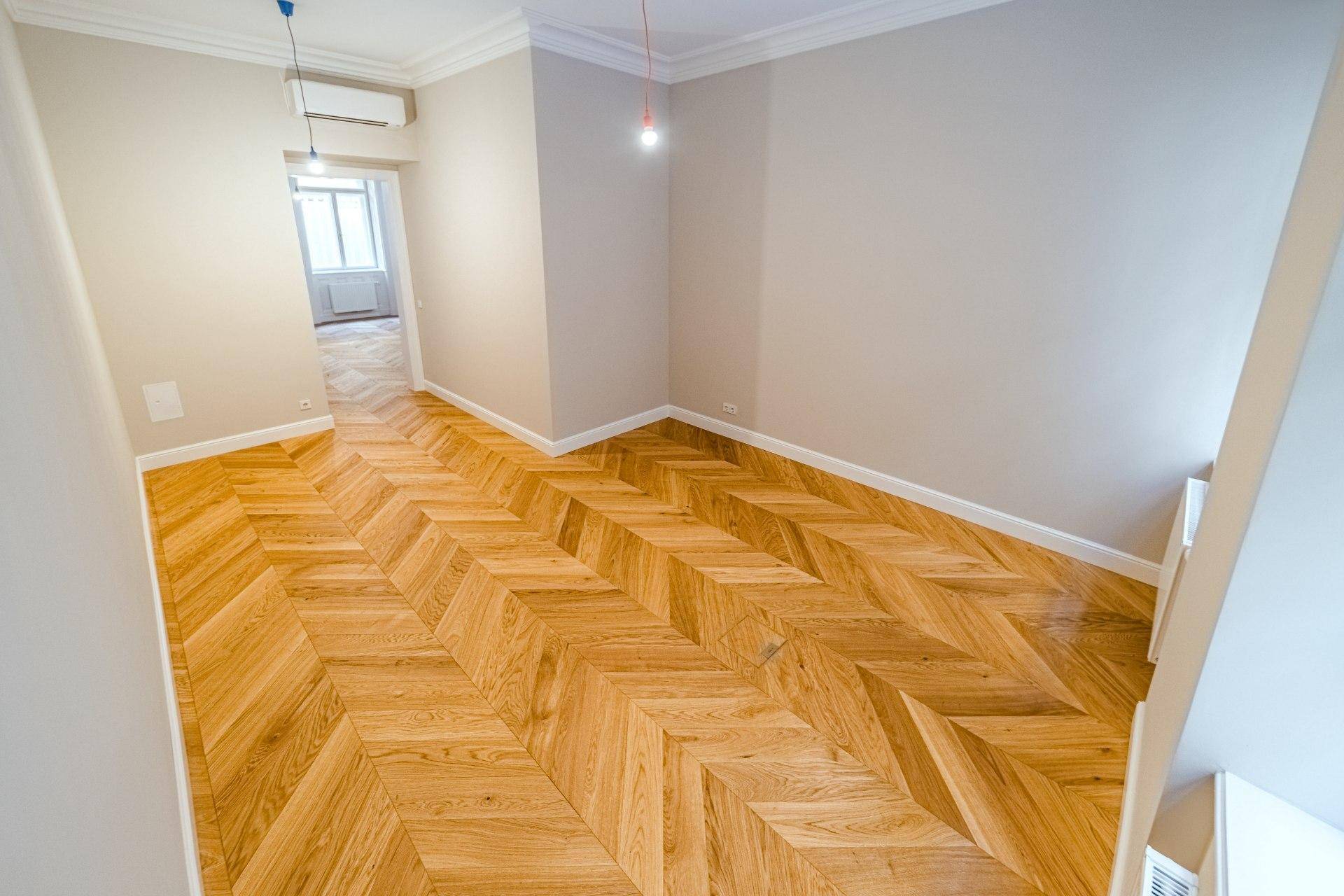 Heller Raum mit Fischgrätparkett und Klimaanlage, der zu einem weiteren Zimmer mit Fenster führt.