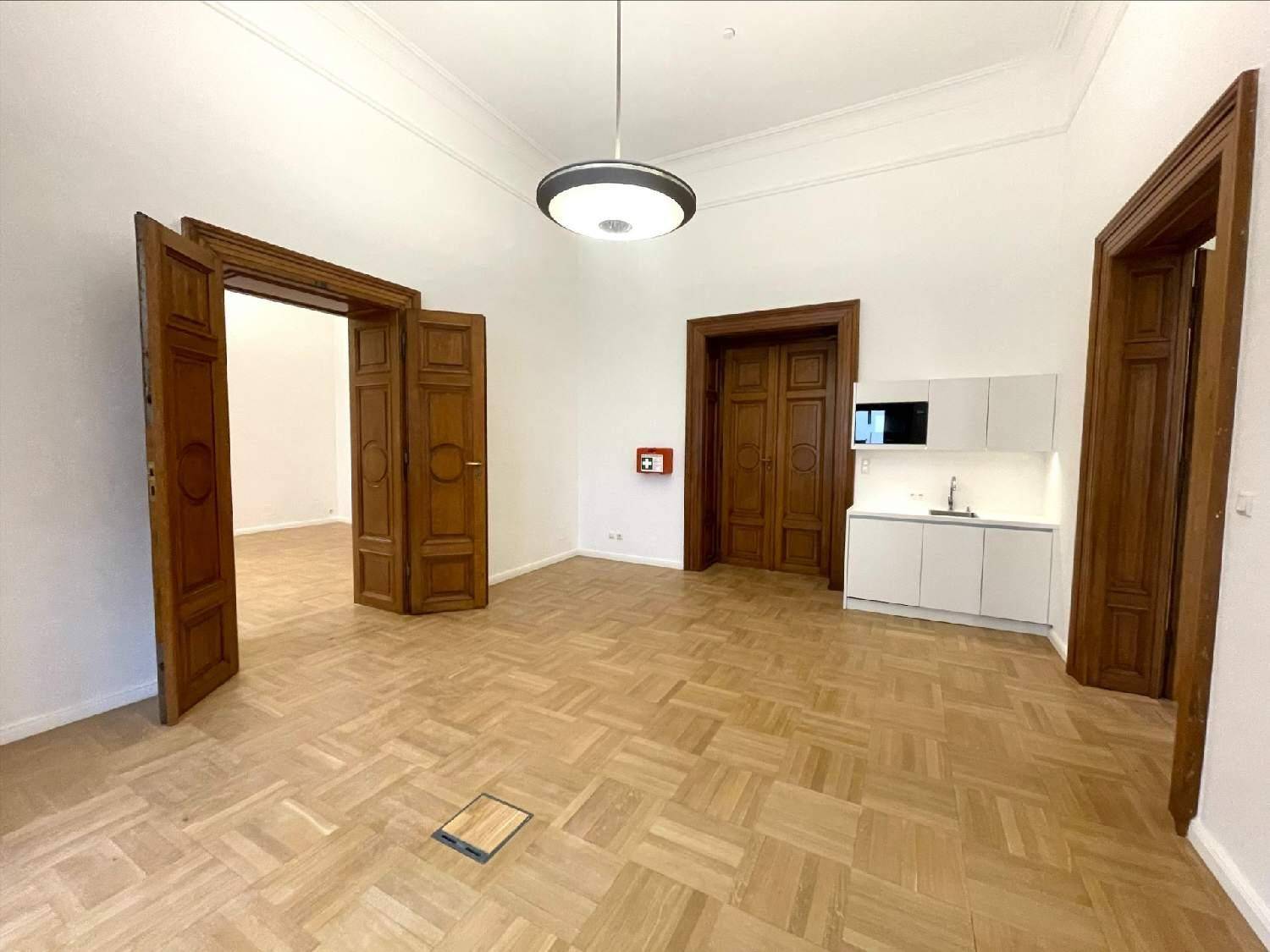 Heller Raum mit Fischgrätparkett, hohen Decken und einer modernen, kompakten Küchenzeile an der Wand.