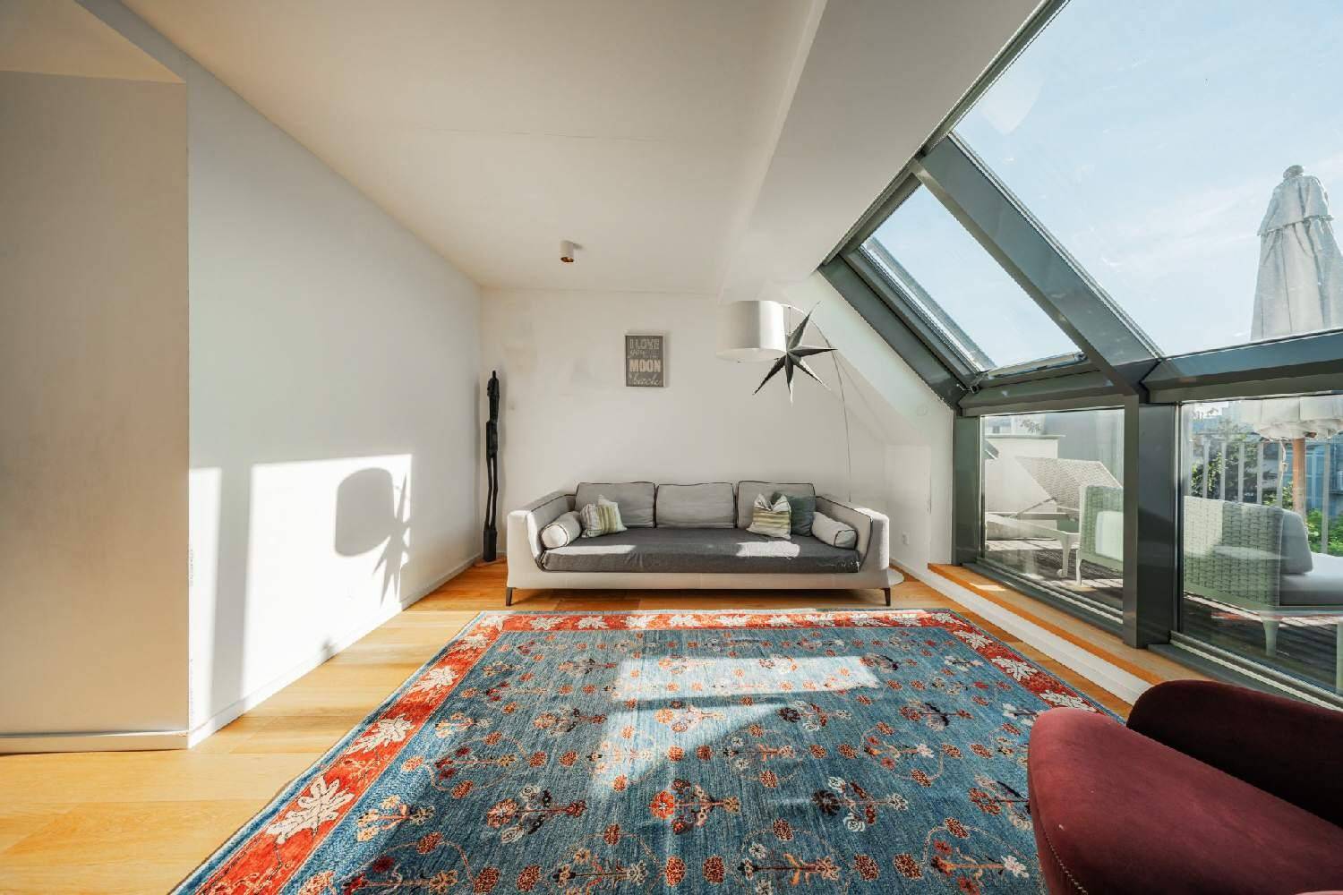 Gemütliches Wohnzimmer mit großem Teppich, Holzboden und viel Tageslicht durch Dachfenster.