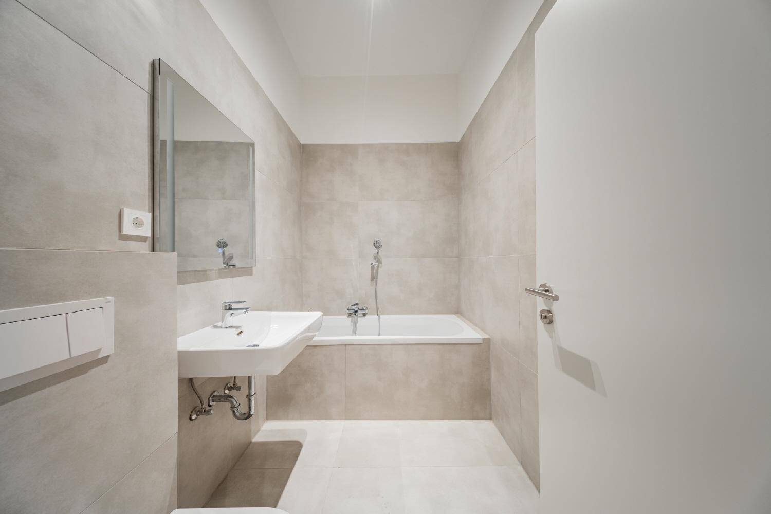 Modernes Badezimmer mit hellen Fliesen, Badewanne, Waschbecken und wandhängendem WC.