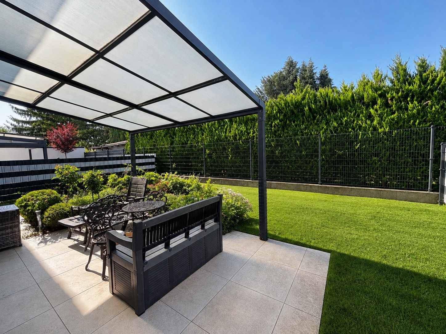 Sonniger Terrassenbereich mit Pergola, Fliesenboden und gepflegtem Garten.