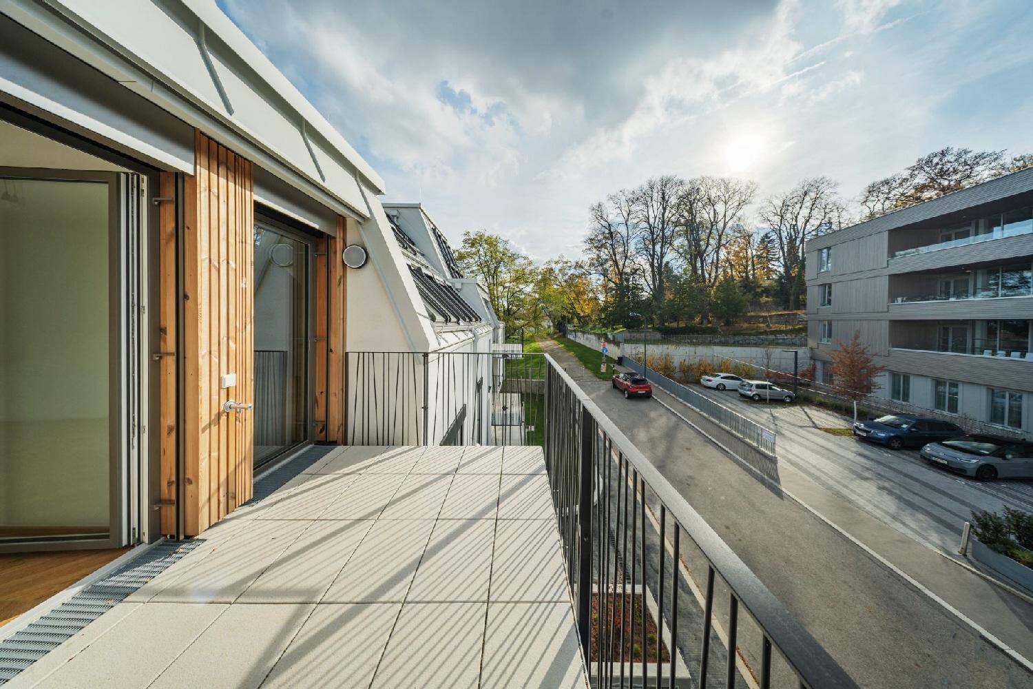 Sonniger Balkon mit Holzelementen und Blick auf die Straße sowie umliegende Bäume.