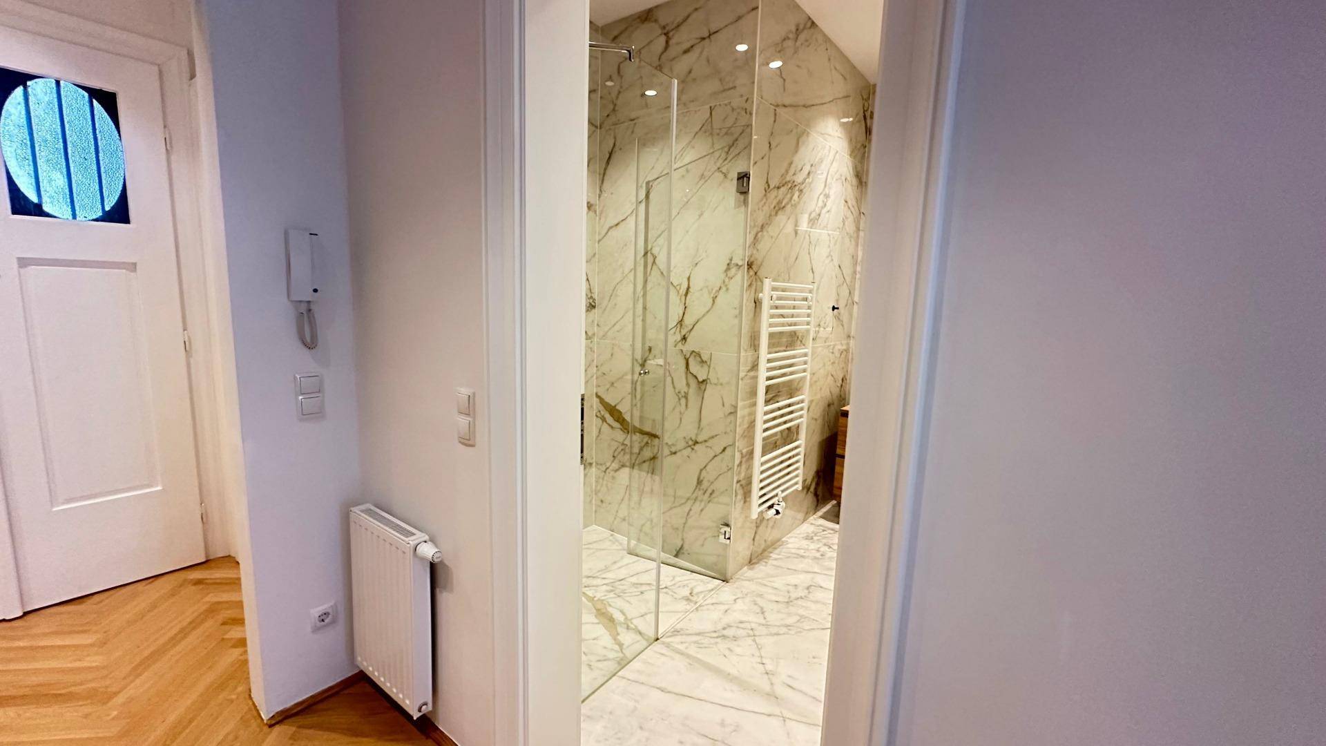 Flur mit Blick in ein modernes Badezimmer mit Marmorfliesen und begehbarer Dusche.