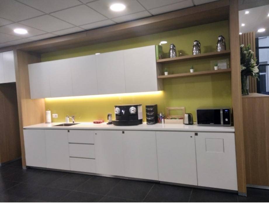 Kleine, moderne Teeküche mit weißen Schränken, Mikrowelle und Kaffeemaschine, ideal für Büropausen.