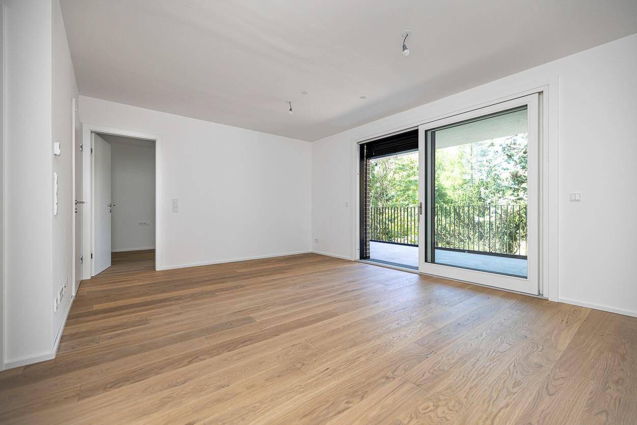 Helles, leeres Wohnzimmer mit Eichenparkett und großem Schiebetürzugang zum Balkon.
