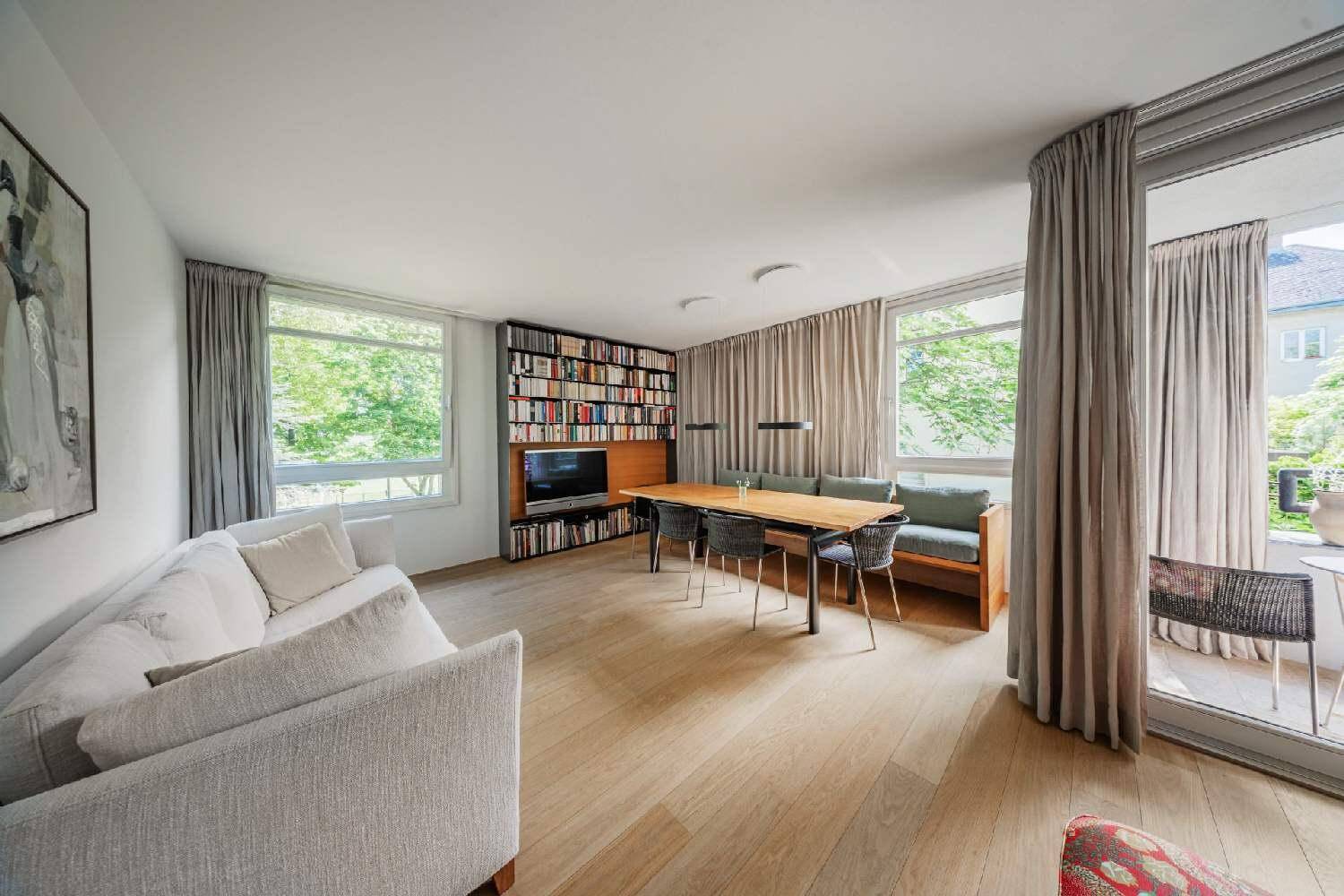 Heller Wohn- und Essbereich mit Holzboden, großem Bücherregal und Zugang zum Balkon.