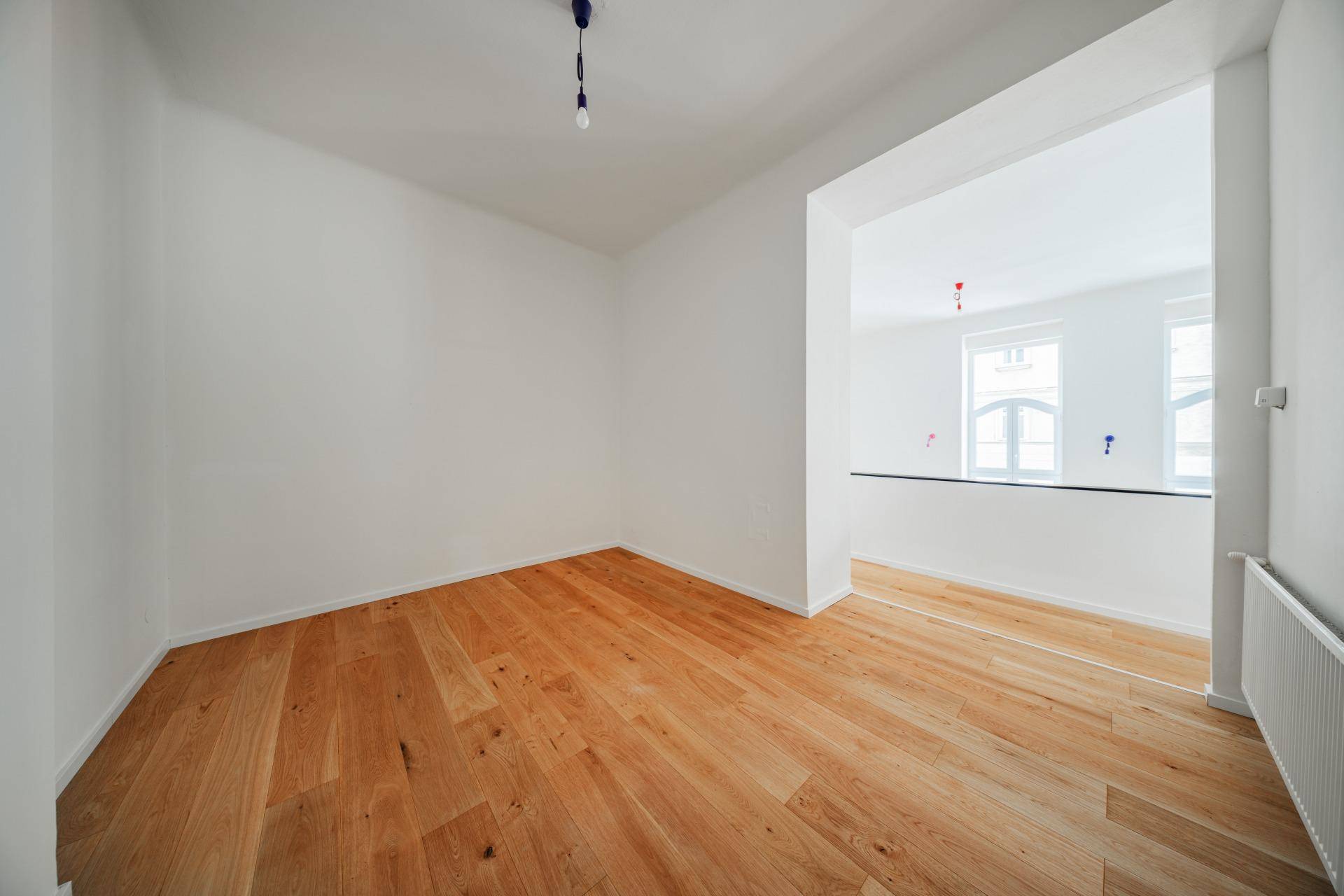 Kleinerer, heller Raum mit Holzboden und offenem Durchgang zu einem größeren Bereich.