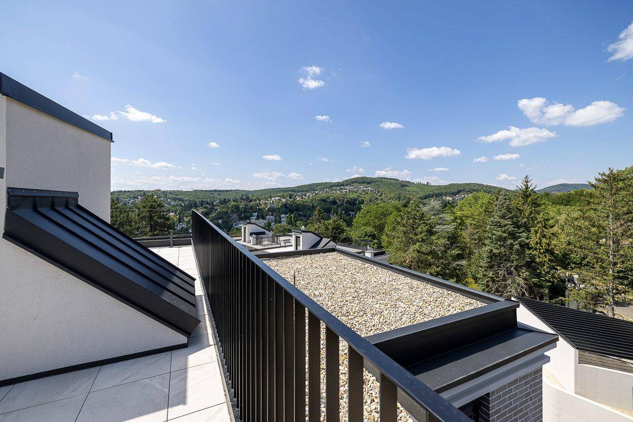 Weitläufiger Blick über die grüne Hügellandschaft von der Dachterrasse eines Neubaus.