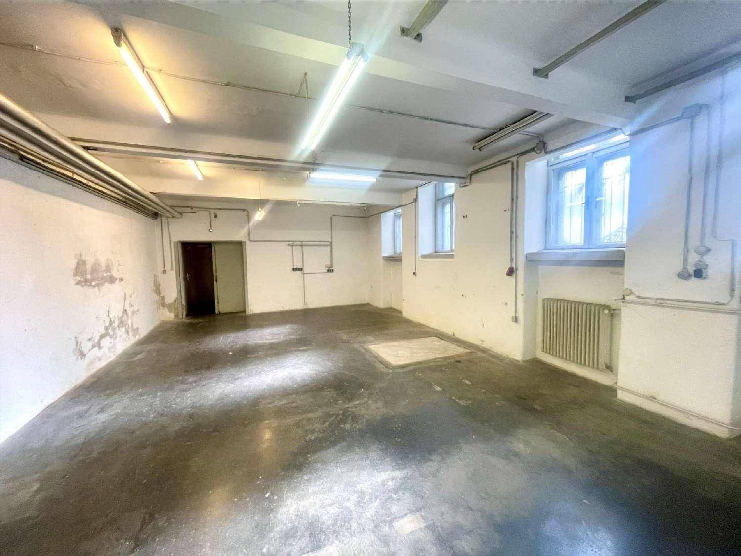Geräumiger, unmöblierter Lagerraum mit hohen Decken, Heizkörpern und sichtbaren Installationen an den Wänden.