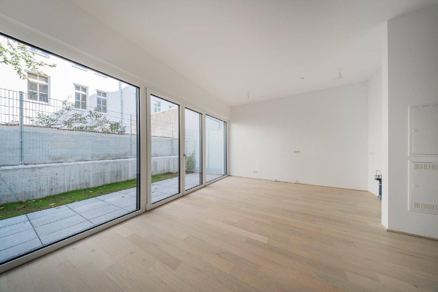 Geräumiger, heller Innenraum mit Holzboden und bodentiefen Fenstern zum Außenbereich.