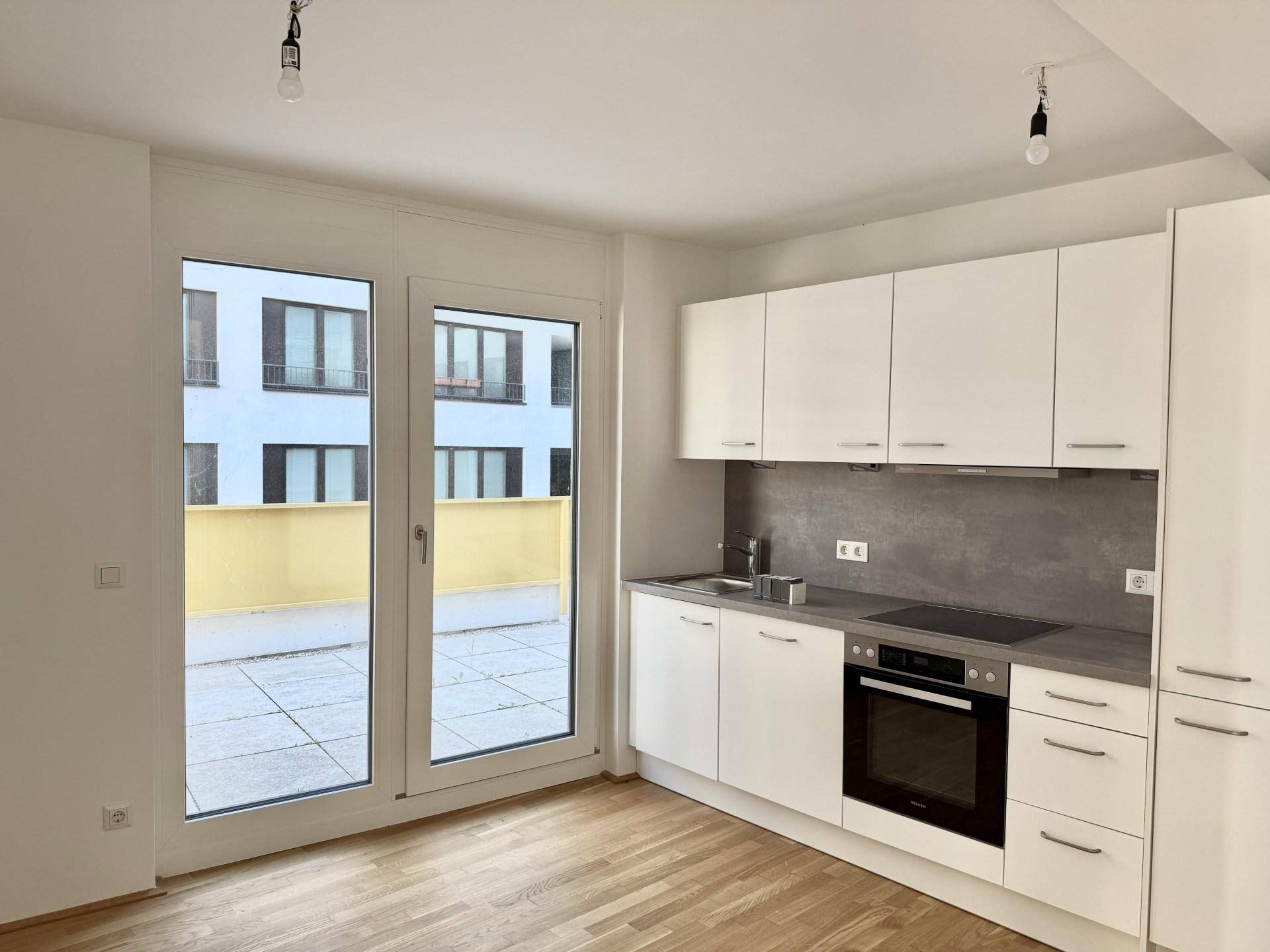 Moderne Einbauküche mit weißen Schränken, Induktionskochfeld und Terrassenzugang.