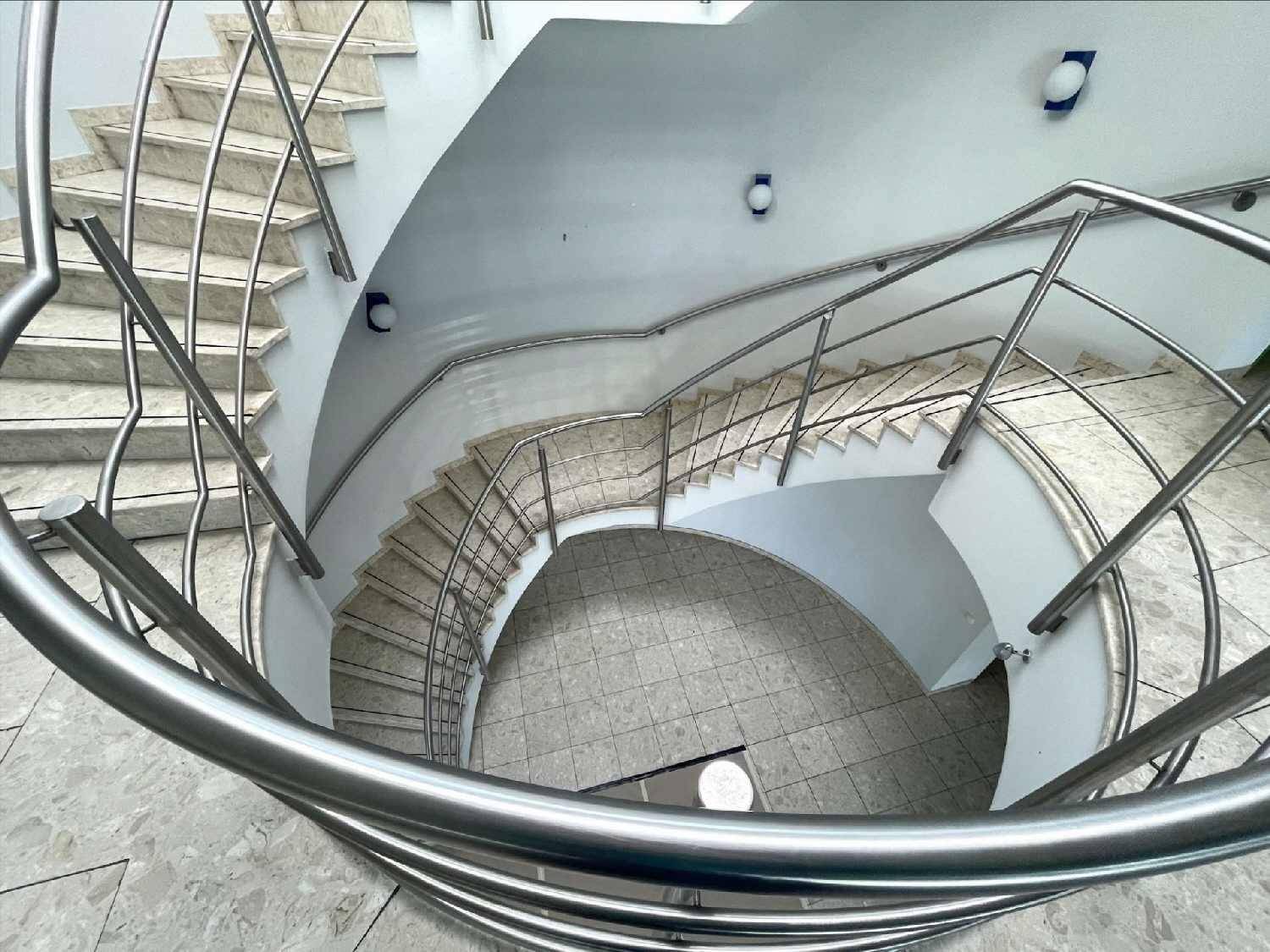 Elegante Wendeltreppe mit Edelstahlgeländer und gefliestem Boden von oben gesehen.