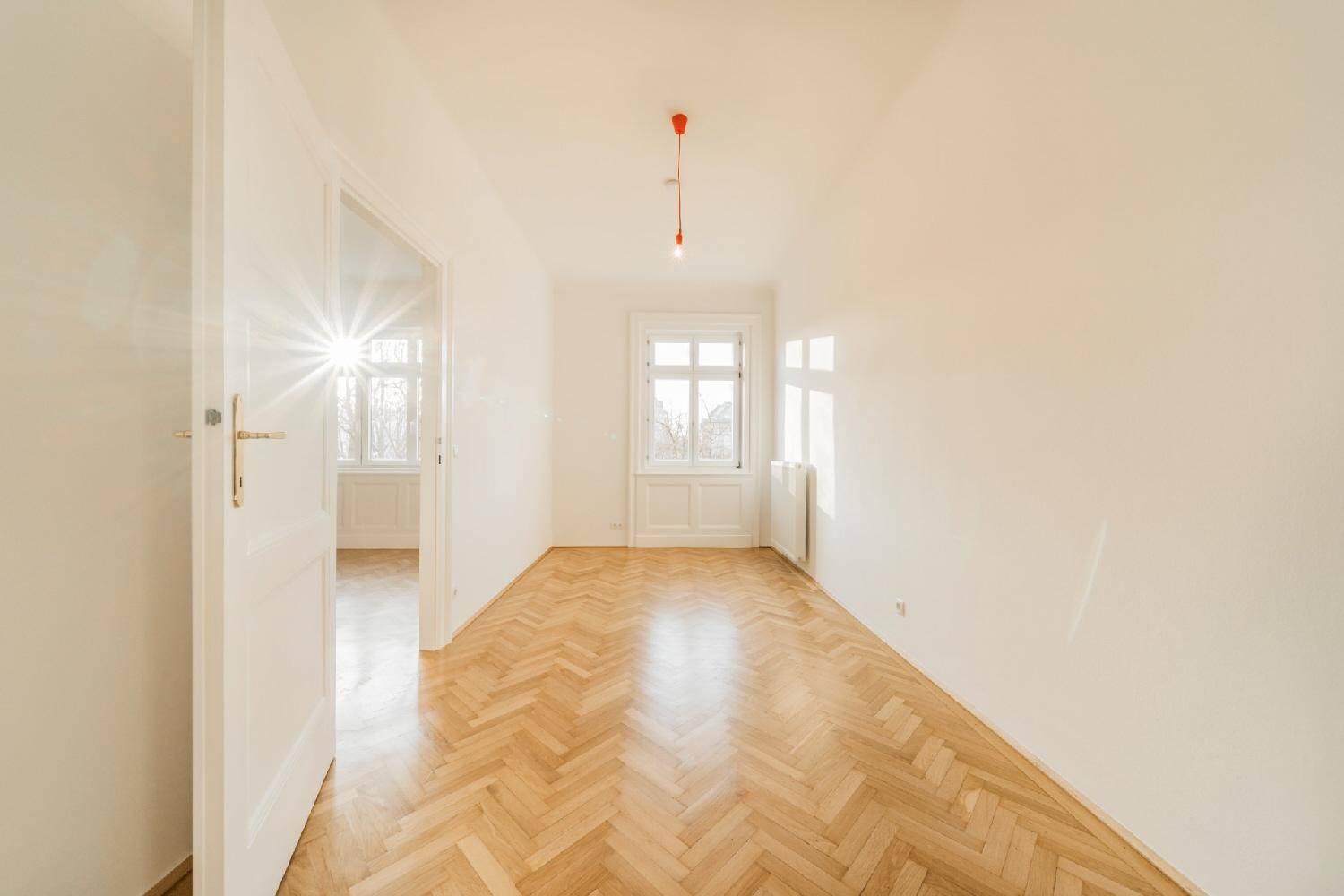 Sonniger Raum mit Fischgrätparkett und einem Fenster, das viel natürliches Licht hereinlässt.